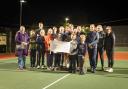 Sidford Tennis Club members on a floodlit court with the giant cheque presented by the SVA