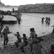 Survivors from HMS Sir Galahad (ablaze in the background) are hauled ashore by colleagues at Bluff Cove, East Falkland, after the ship was hit by an Argentinian air attack on June 8, 1982, during the Falklands Conflict